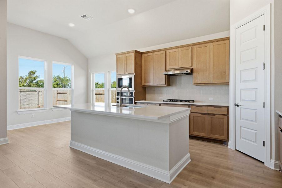 Kitchen with tasteful backsplash, vaulted ceiling, light wood-type flooring, recessed lighting, and a kitchen island with sink Kitchen with tasteful backsplash, vaulted ceiling, light wood-type flooring, recessed lighting, and a kitchen island with sink