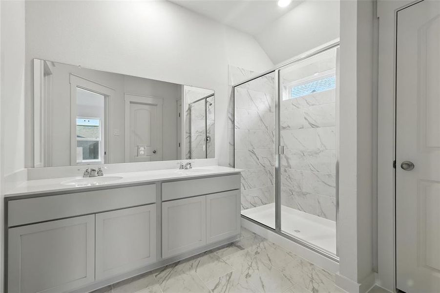 Bathroom featuring a marble finish shower, double vanity, vaulted ceiling, and marble look tile flooring