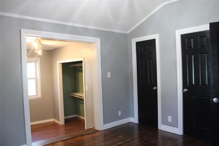 Unfurnished bedroom featuring dark wood-style flooring, vaulted ceiling, and multiple closets Unfurnished bedroom featuring dark wood-style flooring, vaulted ceiling, and multiple closets