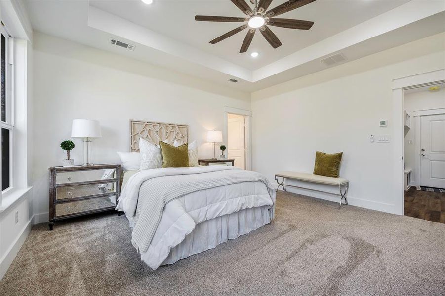 This home's split layout makes for a serene and private primary suite with dramatic tray ceiling and rustic ceiling fan creates an elevated retreat.