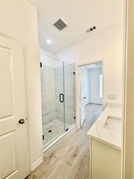Bathroom with light wood finished floors, a marble finish shower, and vanity