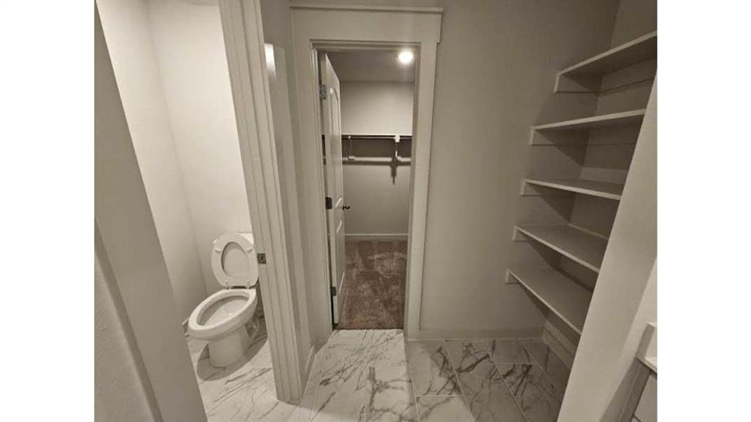 White marble-look tile flooring leading to a separate water closet and a built-in shelving unit