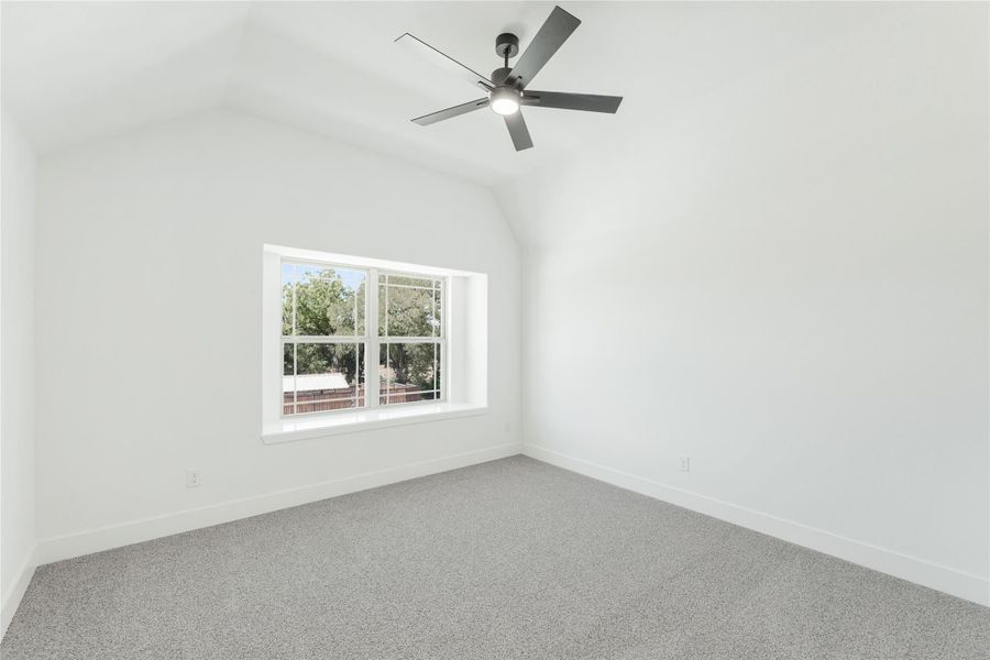 Empty bedroom with vaulted ceiling, ceiling fan, gray carpet, and large window Empty bedroom with vaulted ceiling, ceiling fan, gray carpet, and large window