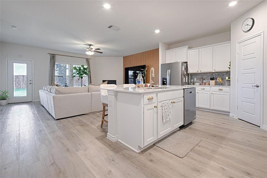 Kitchen featuring ceiling fan, stainless steel appliances, white cabinets, light wood-type flooring, and a kitchen island with sink