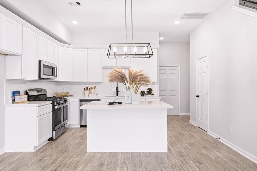 Spacious kitchen features upgraded cabinetry, crown molding, quartz countertops, stainless steel appliances, and a center island with pendant lights and bar-top seating.