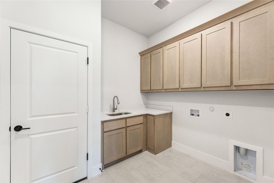 Laundry room with light wood upper cabinets, utility sink, and washer and dryer hookups on white walls