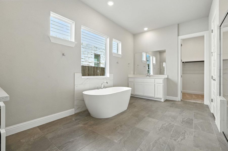 Full bathroom with vanity, a freestanding bath, a walk in closet, and recessed lighting