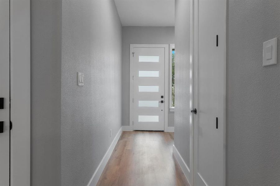 Doorway with light wood-style flooring, baseboards, and a textured wall