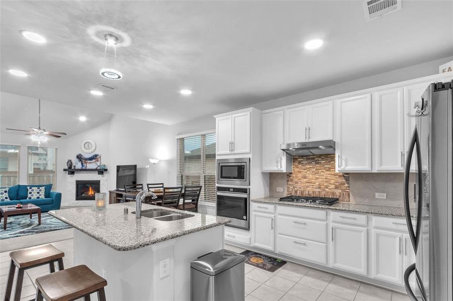 Kitchen featuring under cabinet range hood, white cabinets, open floor plan, appliances with stainless steel finishes, and a glass covered fireplace