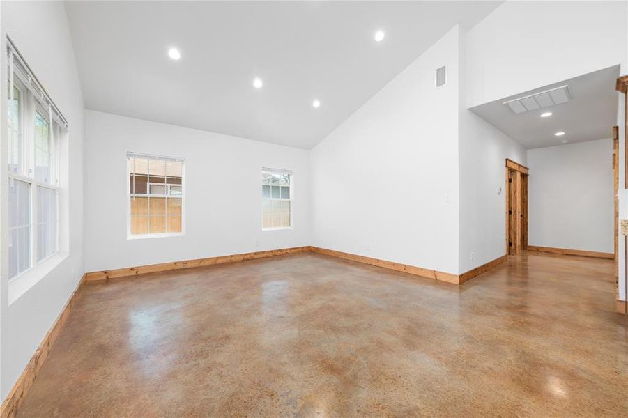 Empty room with high vaulted ceiling, finished concrete flooring, baseboards, visible vents, and recessed lighting Empty room with high vaulted ceiling, finished concrete flooring, baseboards, visible vents, and recessed lighting