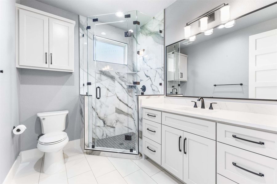 Full bath with vanity, toilet, a marble finish shower, tile patterned flooring, and baseboards Full bath with vanity, toilet, a marble finish shower, tile patterned flooring, and baseboards