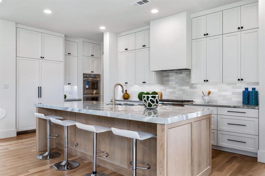 Kitchen featuring backsplash, light stone counters, a kitchen island with sink, stainless steel appliances, and hardwood / wood-style floors