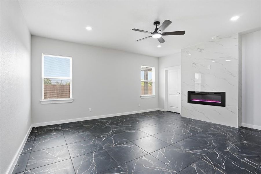 Spacious room featuring large format black marble-look tile flooring, a contemporary ceiling fan with integrated lighting, recessed lighting, and a prominent white marble-look fireplace with an electric insert