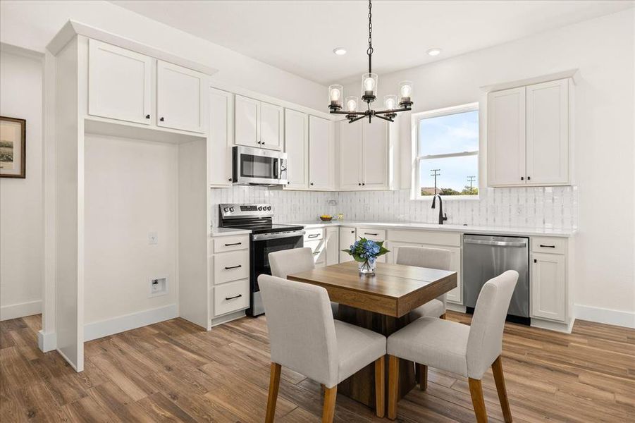 Contemporary kitchen featuring white cabinetry, stainless steel appliances, wood-finish flooring, and a window above the sink