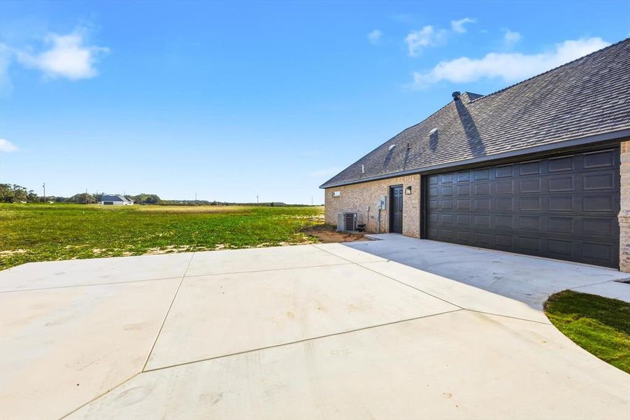 View of home's exterior with concrete driveway, brick siding, a shingled roof, a yard, and an attached garage