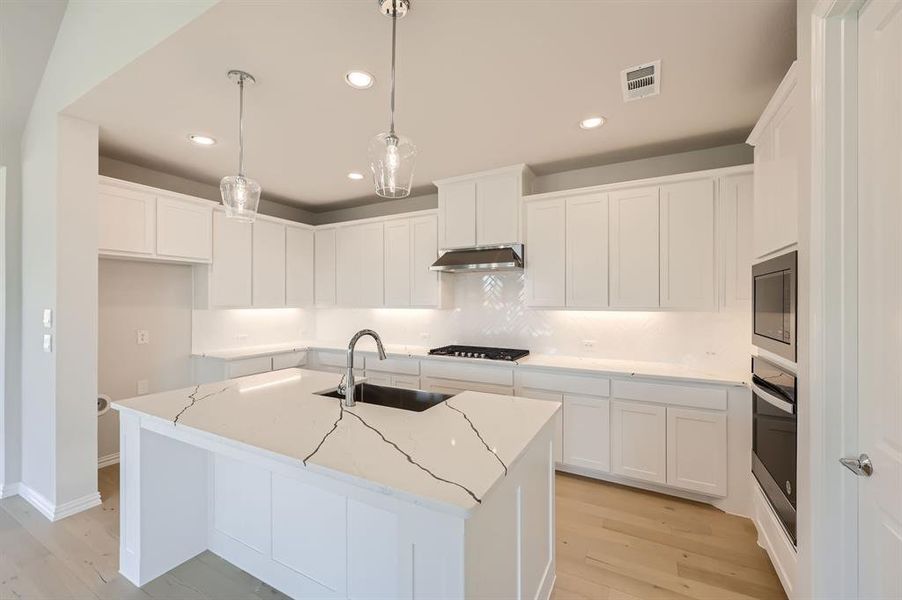 Kitchen featuring sink, light wood-type flooring, stainless steel appliances, white cabinets, and a center island with sink