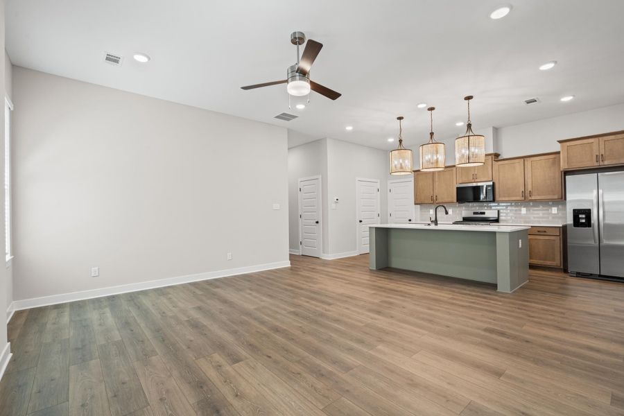 Kitchen featuring stainless steel appliances, brown cabinetry, an island with sink, decorative backsplash, and hanging light fixtures
