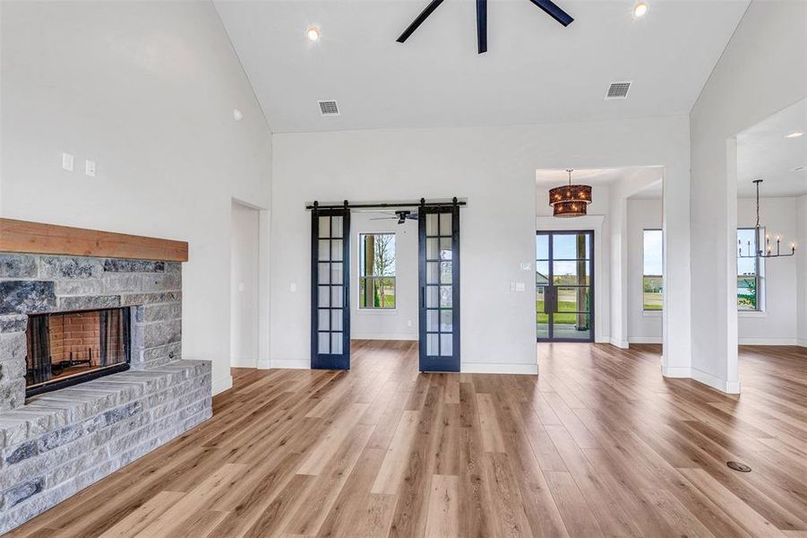 Unfurnished living room featuring french doors, ceiling fan with notable chandelier, high vaulted ceiling, a fireplace, and hardwood / wood-style floors