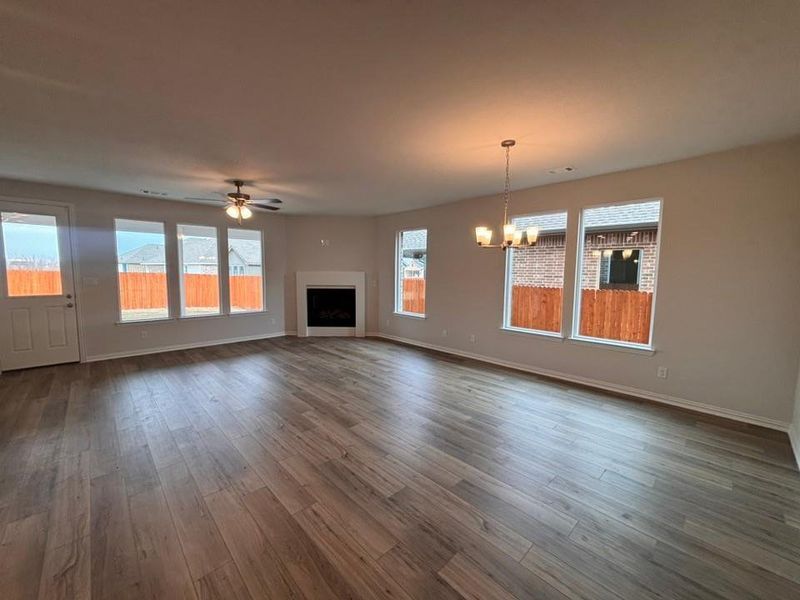 Unfurnished living room with a fireplace, wood finished floors, a chandelier, and ceiling fan Unfurnished living room with a fireplace, wood finished floors, a chandelier, and ceiling fan