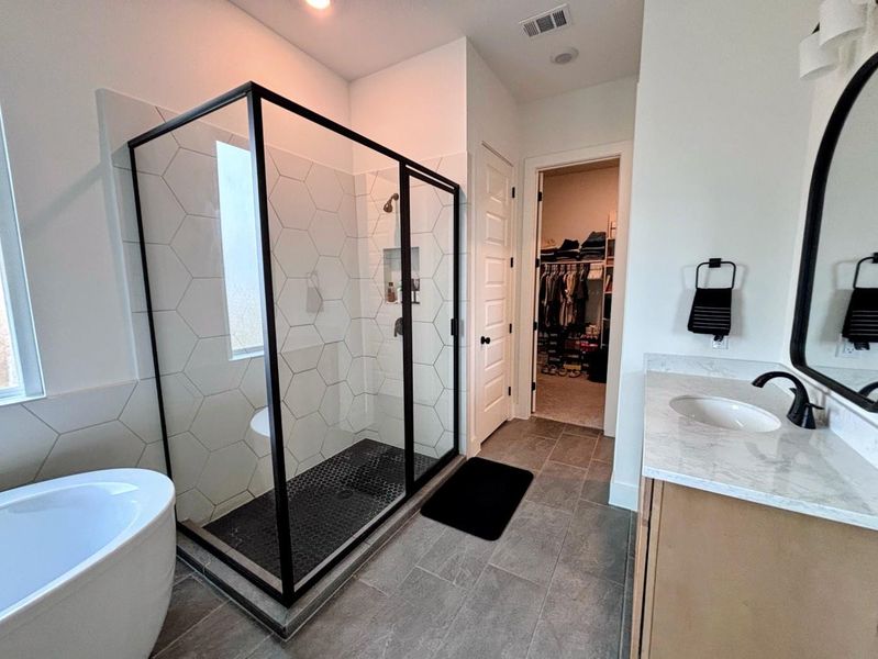 Modern master bathroom with a spacious glass-enclosed shower, stylish hexagonal tiles, a freestanding bathtub, and dual sinks. Adjacent is a walk-in closet with ample storage.