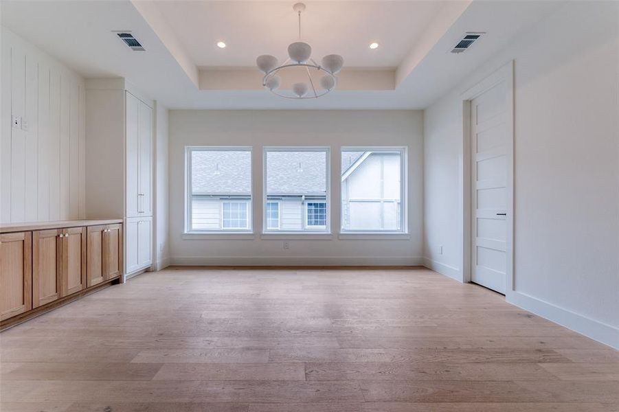 Spare room featuring baseboards, light wood-style floors, a tray ceiling, and a chandelier Spare room featuring baseboards, light wood-style floors, a tray ceiling, and a chandelier