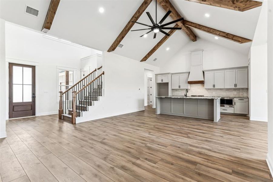 Unfurnished living room featuring kitchen island, light wood-type flooring, beam ceiling, high vaulted ceiling, and ceiling fan