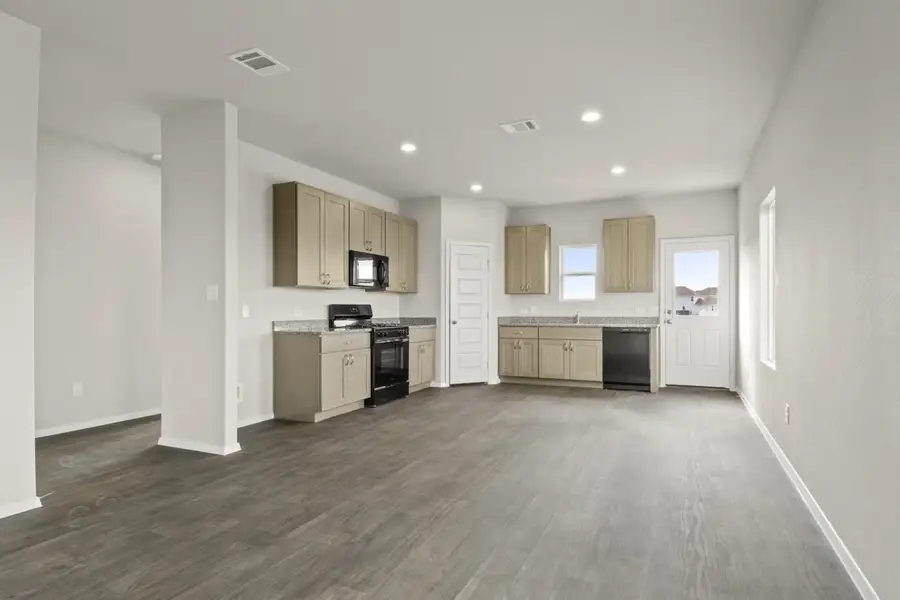 Image of kitchen with brown flooring and light grey walls with light brown cabinets and black stove