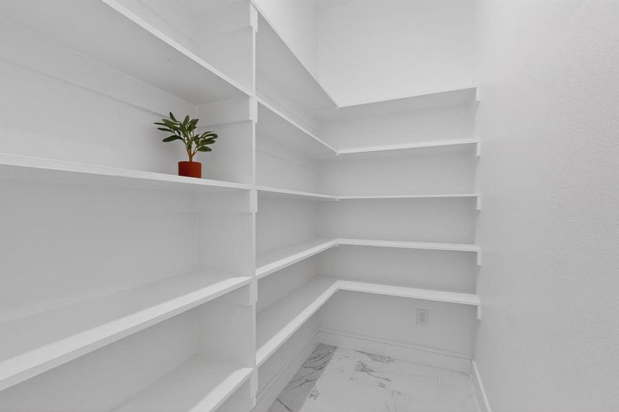 Expansive corner pantry featuring multiple levels of white shelving, white walls, and a light-toned, veined tile flooring