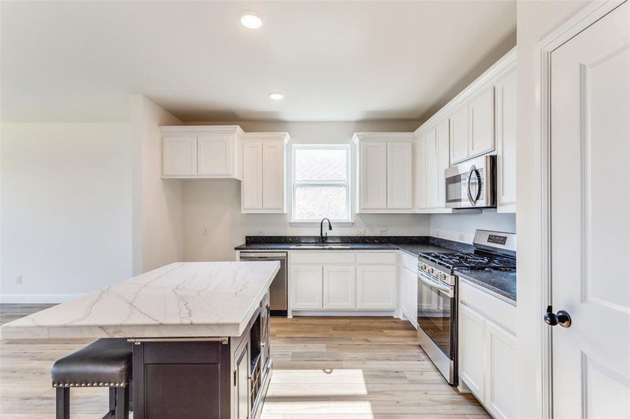 Kitchen featuring light hardwood / wood-style flooring, white cabinets, a kitchen island, stainless steel appliances, and sink