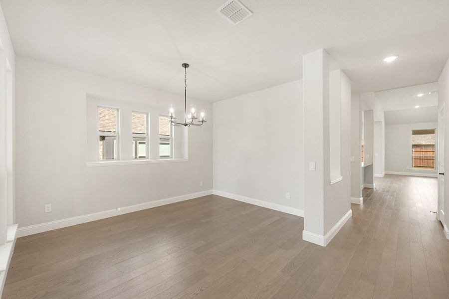 Empty dining room with chandelier, hardwood floors, and white walls open to hallway