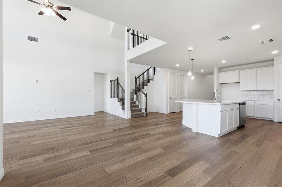 Kitchen featuring open floor plan, white cabinets, a center island with sink, dark wood-style floors, and a high ceiling