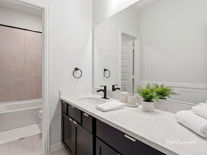 Full bath featuring a vanity with stone-look countertop and a large framed mirror. A tub-and-shower combination with tile surround and crisp wainscoting detailing round out the space. This photo has been digitally staged to illustrate the possibilities of the home's aesthetic and potential design. Some furnishings and décor shown are for visual inspiration.