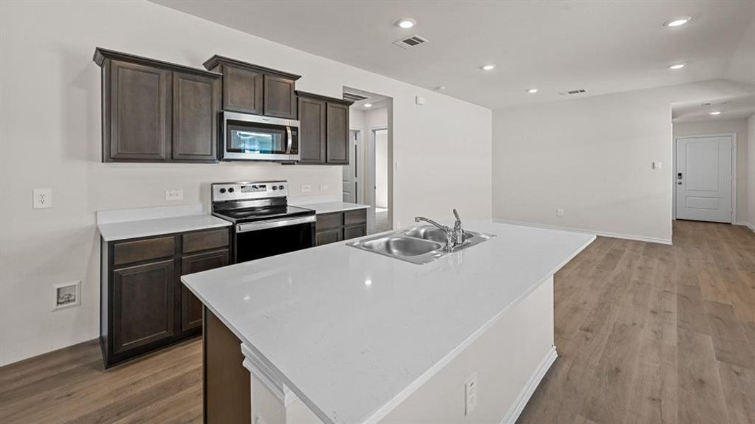 Kitchen featuring dark wood cabinetry, white countertops, stainless steel appliances, and a central island with an integrated double sink
