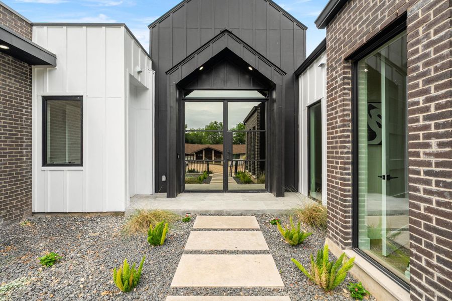 Modern architectural facade featuring dark brick, white vertical siding, a black metal roofline, and a prominent glass entry door