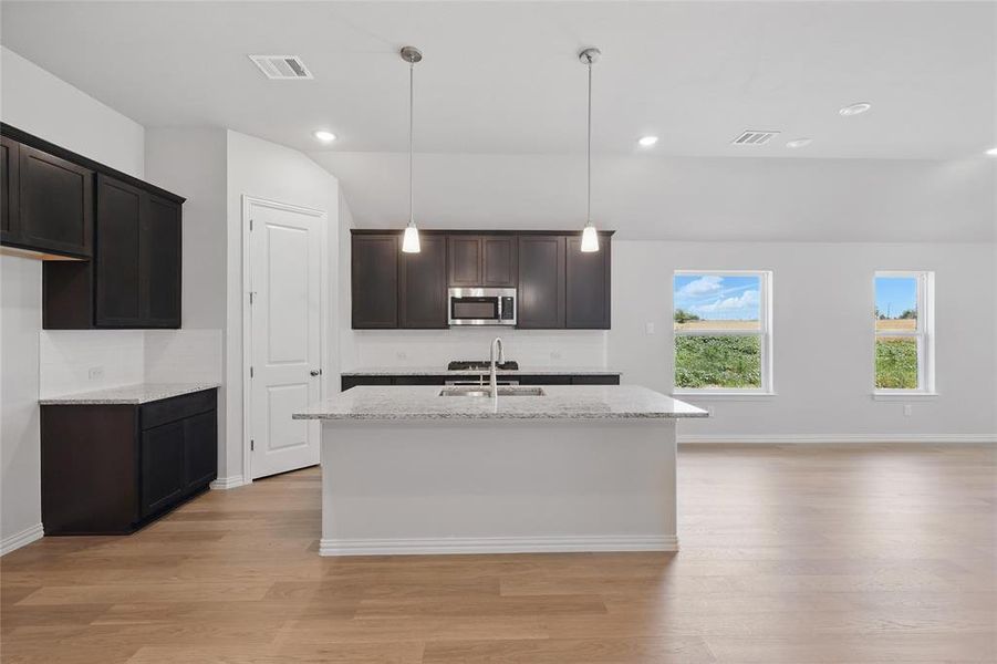 Kitchen with stainless steel microwave, a sink, light wood-style floors, a kitchen island with sink, and light stone countertops