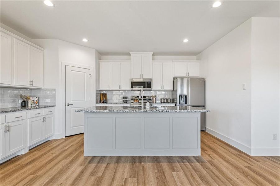 Kitchen with light stone countertops, appliances with stainless steel finishes, light wood-type flooring, and a kitchen island with sink Kitchen with light stone countertops, appliances with stainless steel finishes, light wood-type flooring, and a kitchen island with sink