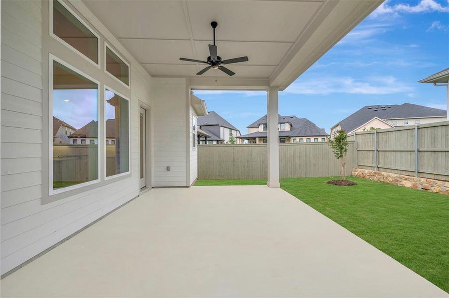 The property features an expansive covered patio with a ceiling fan, overlooking a verdant lawn and a wooden fence