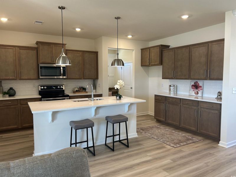 Kitchen with backsplash, stainless steel appliances, a kitchen breakfast bar, light wood-type flooring, and pendant lighting