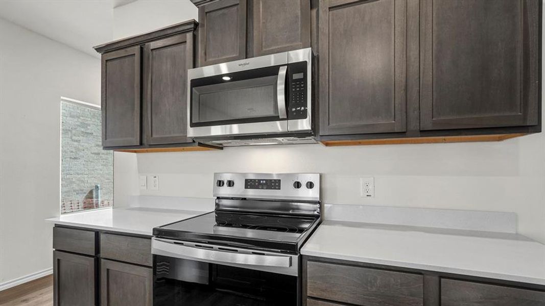 Kitchen featuring dark wood cabinetry, white countertops, and stainless steel appliances including a microwave and an electric range