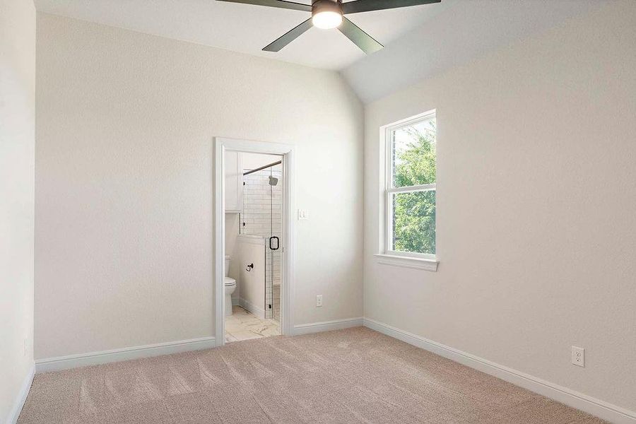 Unfurnished bedroom with light colored carpet, ensuite bath, ceiling fan, and vaulted ceiling