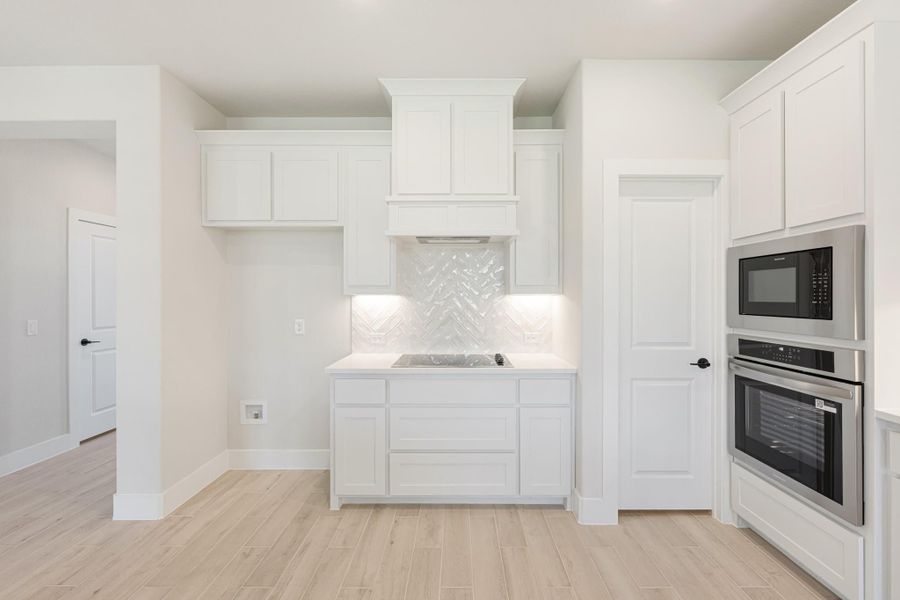White kitchen with herringbone tile backsplash, built-in oven, microwave, and light wood-look floors