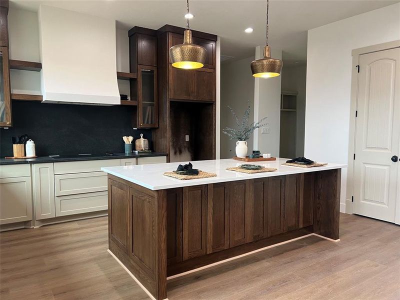 Kitchen featuring tasteful backsplash, a center island, dark brown cabinets, hanging light fixtures, and light hardwood / wood-style flooring