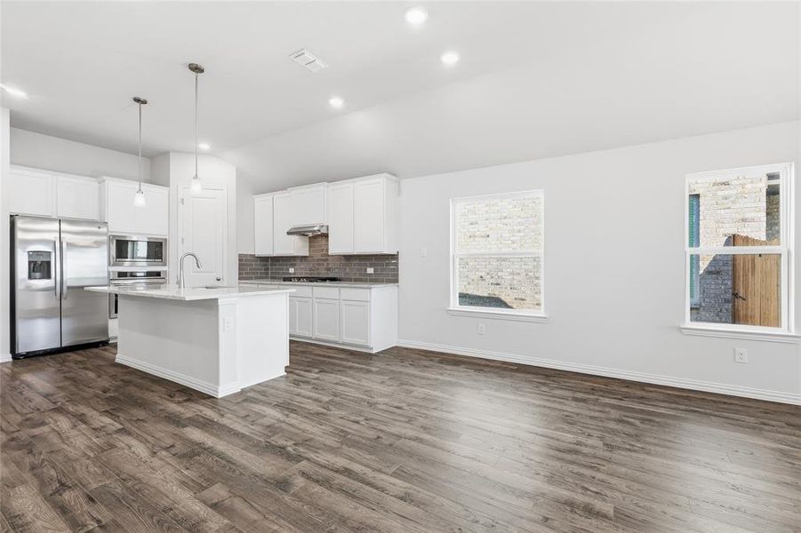 Open-concept kitchen and living area featuring wood-finish flooring, recessed lighting, and a white kitchen island with pendant lighting
