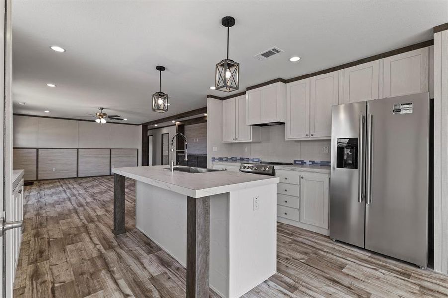 Kitchen featuring stainless steel appliances, light countertops, hanging light fixtures, a kitchen island with sink, and light wood finished floors