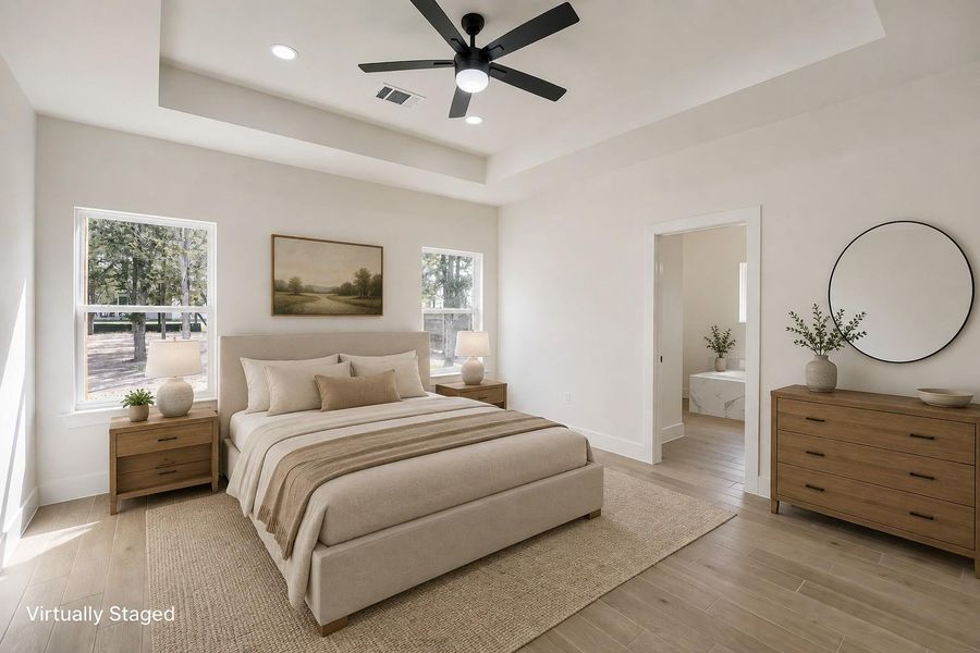 Recessed lighting illuminates this bright bedroom, featuring a tray ceiling and a ceiling fan for optimal comfort.