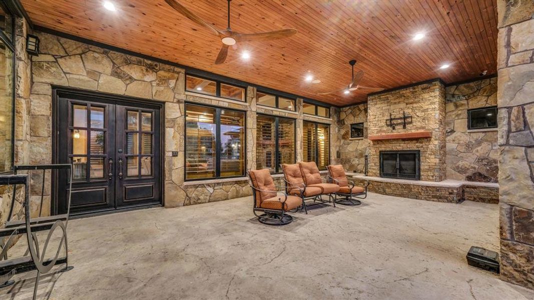 Outdoor living area with stone fireplace, wood ceiling, and multiple seating options for year-round enjoyment.