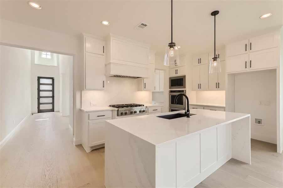 Kitchen featuring a center island with sink, light hardwood / wood-style flooring, appliances with stainless steel finishes, sink, and custom exhaust hood