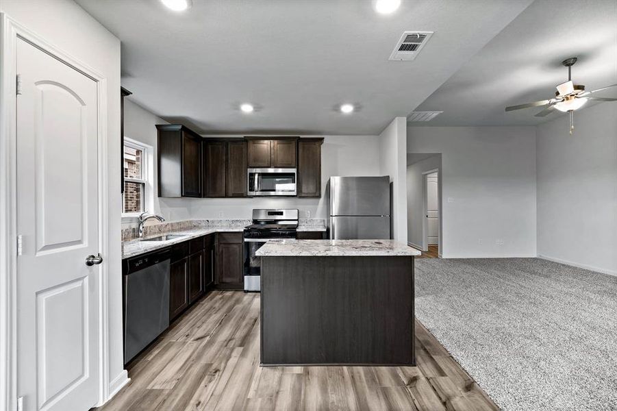 Kitchen featuring ceiling fan, light carpet, a kitchen island, dark brown cabinetry, and appliances with stainless steel finishes