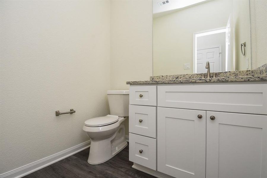 A clean, modern bathroom interior with white cabinetry, granite countertop, and a toilet next to a textured wall.