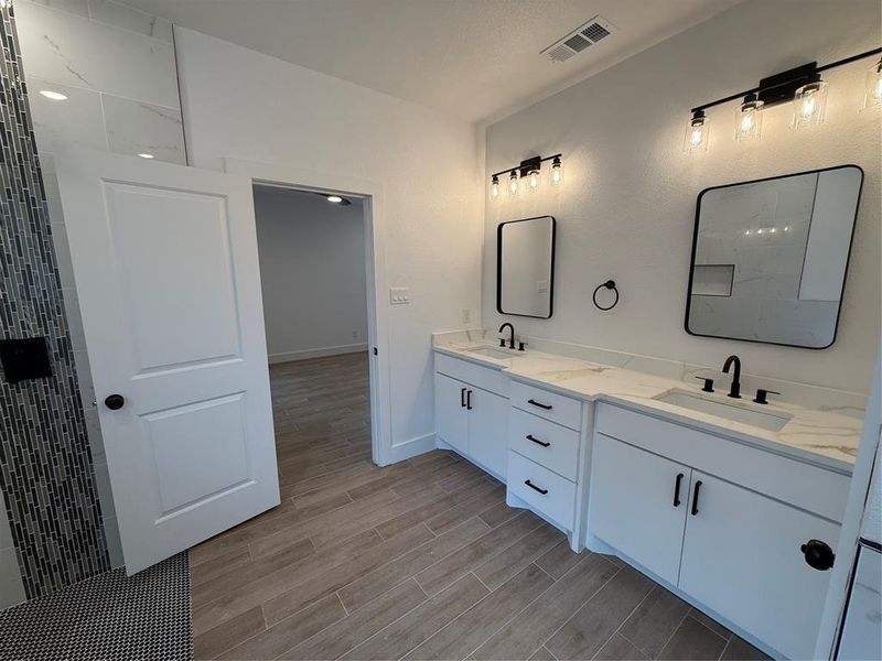 Full bathroom featuring wood finish floors, double vanity, and tiled shower Full bathroom featuring wood finish floors, double vanity, and tiled shower
